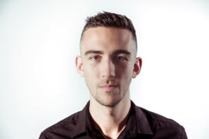 George has brown hair and is looking at the camera half smiling.  There is a white background