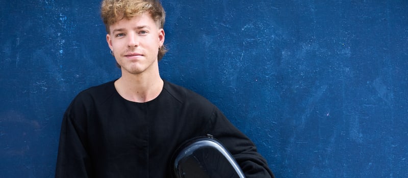 James Morley, cellist, with cello case on a blue background