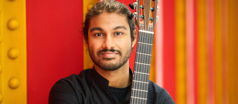 Samrat Majumder (guitarist) with guitar resting on his shoulder in front of a yellow and red background