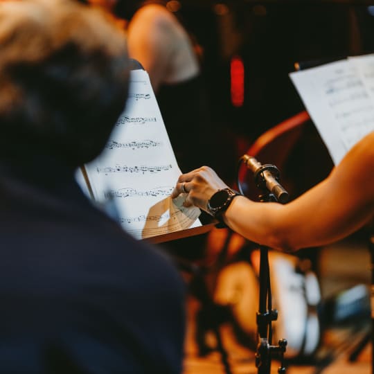 A musician sitting in the orchestra turns a page of music