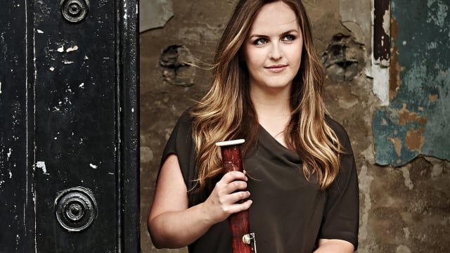 Amy Harman with bassoon standing by black door